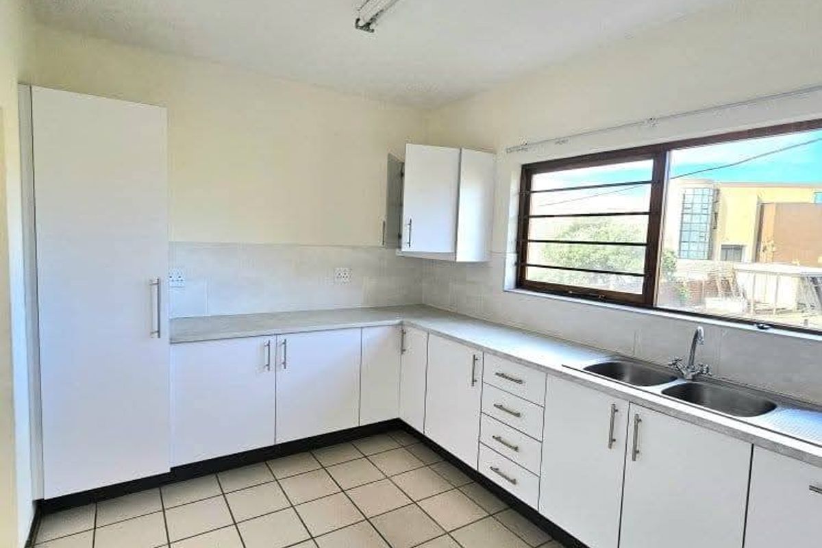 A functional, empty kitchen featuring white cabinetry, laminate countertops, a double basin sink, and tiled flooring, offering a clean canvas for potential updates.