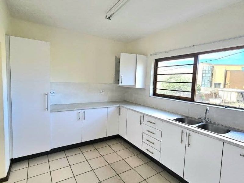 A functional, empty kitchen featuring white cabinetry, laminate countertops, a double basin sink, and tiled flooring, offering a clean canvas for potential updates.