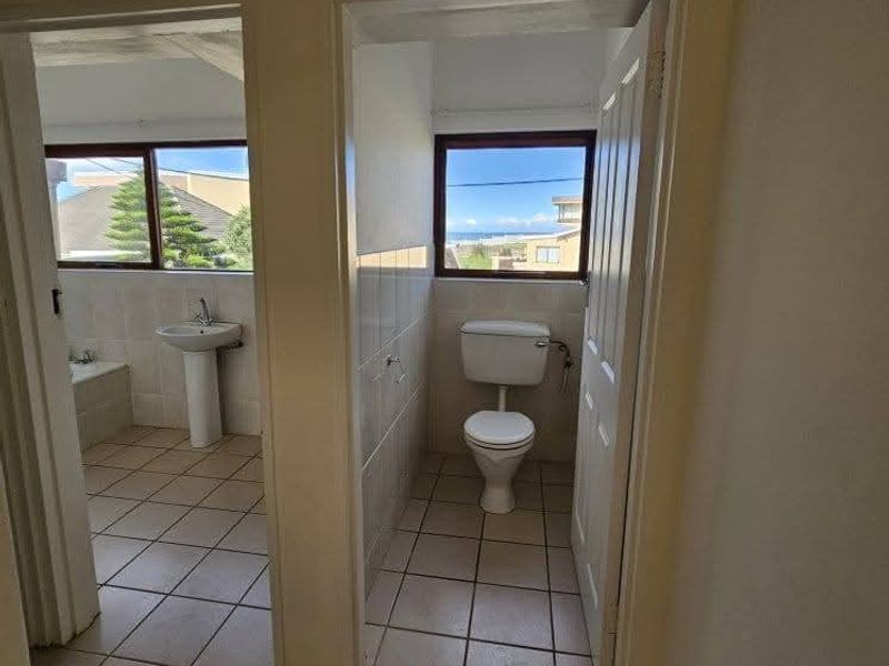 A dated bathroom featuring a separate toilet room and a main area with a pedestal sink and built-in bathtub, finished with ceramic tiling.