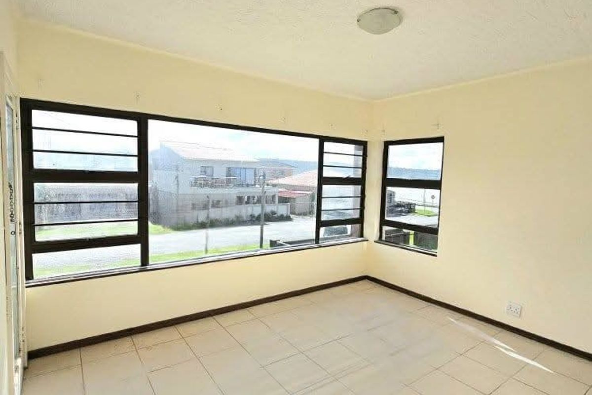 An empty living area featuring large windows with neighbourhood views, ceramic tiled flooring, and neutral walls, offering a blank canvas for renovation.