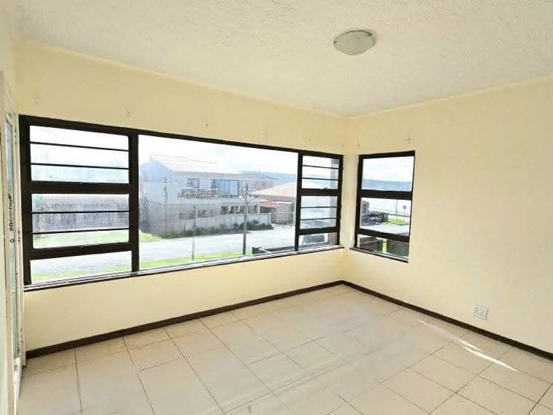 An empty living area featuring large windows with neighbourhood views, ceramic tiled flooring, and neutral walls, offering a blank canvas for renovation.