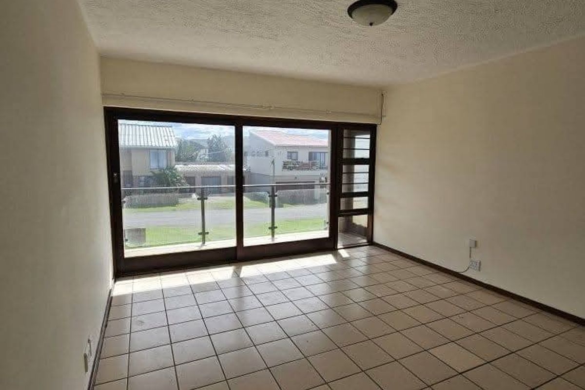 An empty living room featuring large sliding glass doors that open to a balcony, tiled flooring, and a textured ceiling.