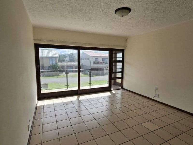 An empty living room featuring large sliding glass doors that open to a balcony, tiled flooring, and a textured ceiling.