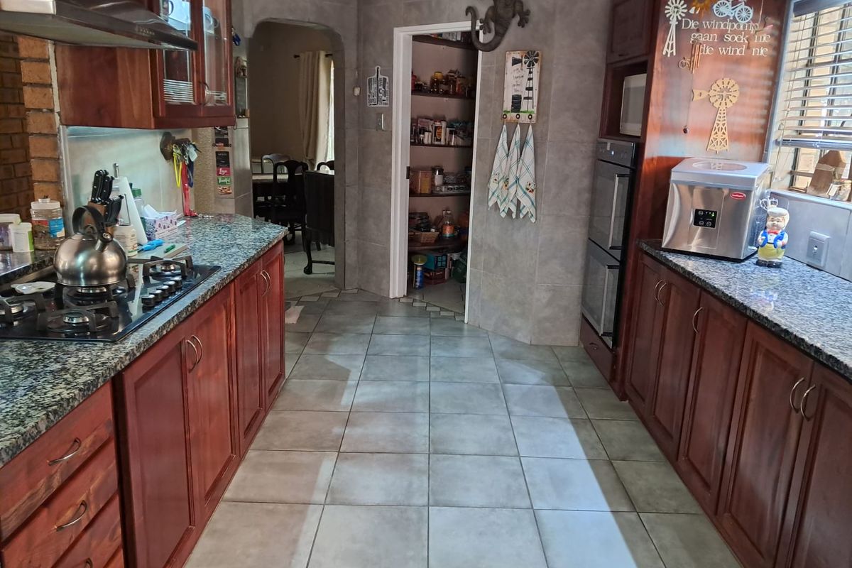 A functional kitchen featuring dark wood cabinetry, granite countertops, a gas hob, built-in double oven, and an adjacent walk-in pantry.