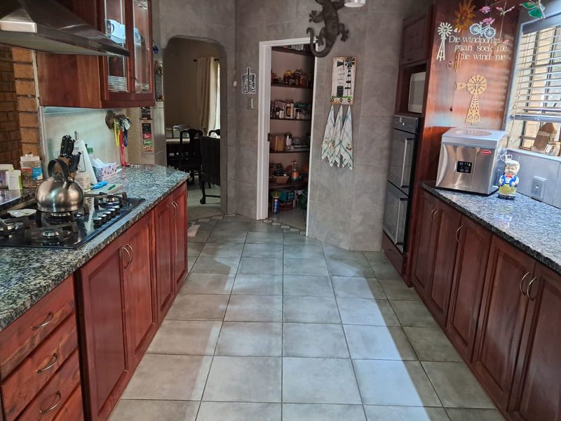 A functional kitchen featuring dark wood cabinetry, granite countertops, a gas hob, built-in double oven, and an adjacent walk-in pantry.