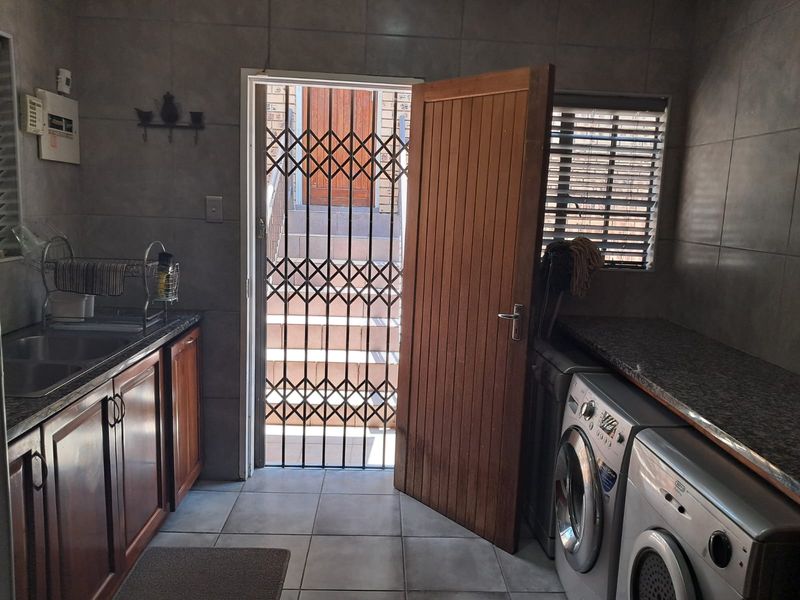 Functional laundry room featuring built-in cabinetry, granite countertops, a stainless steel sink, and direct access to the exterior via a security gate.