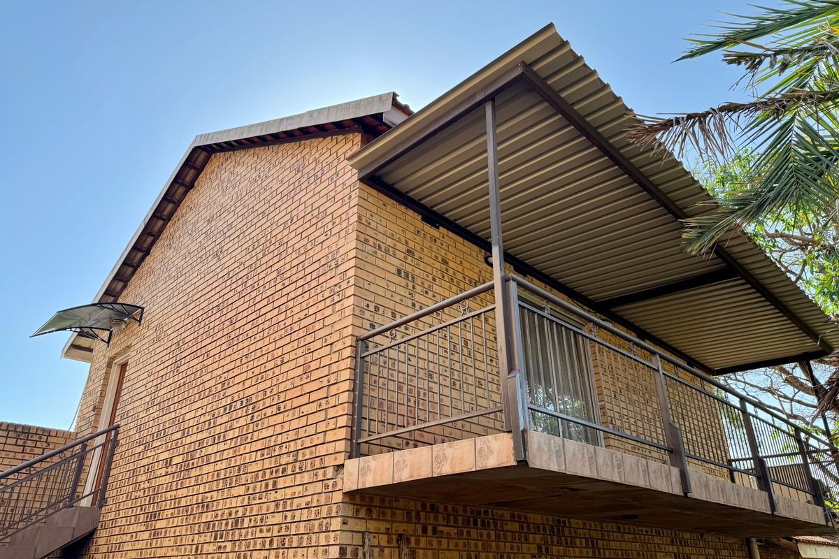 Rear view of a face brick house featuring an elevated balcony with metal railings and a corrugated metal roof covering.