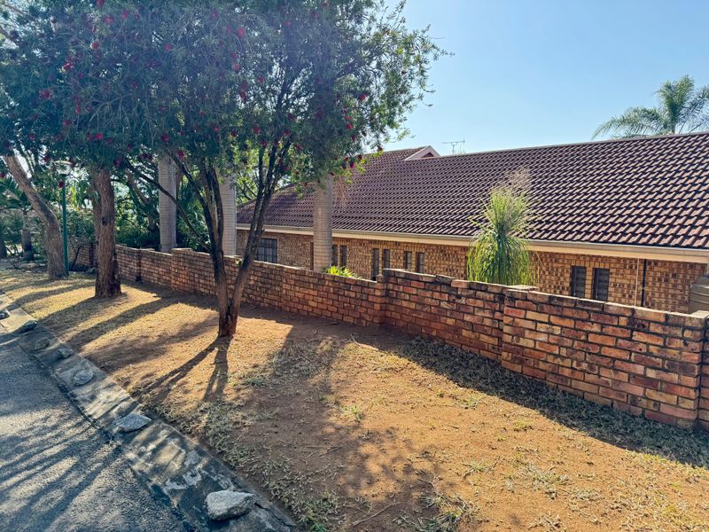 A view of the property exterior featuring a face brick facade, tiled roof, and a boundary wall with established trees.