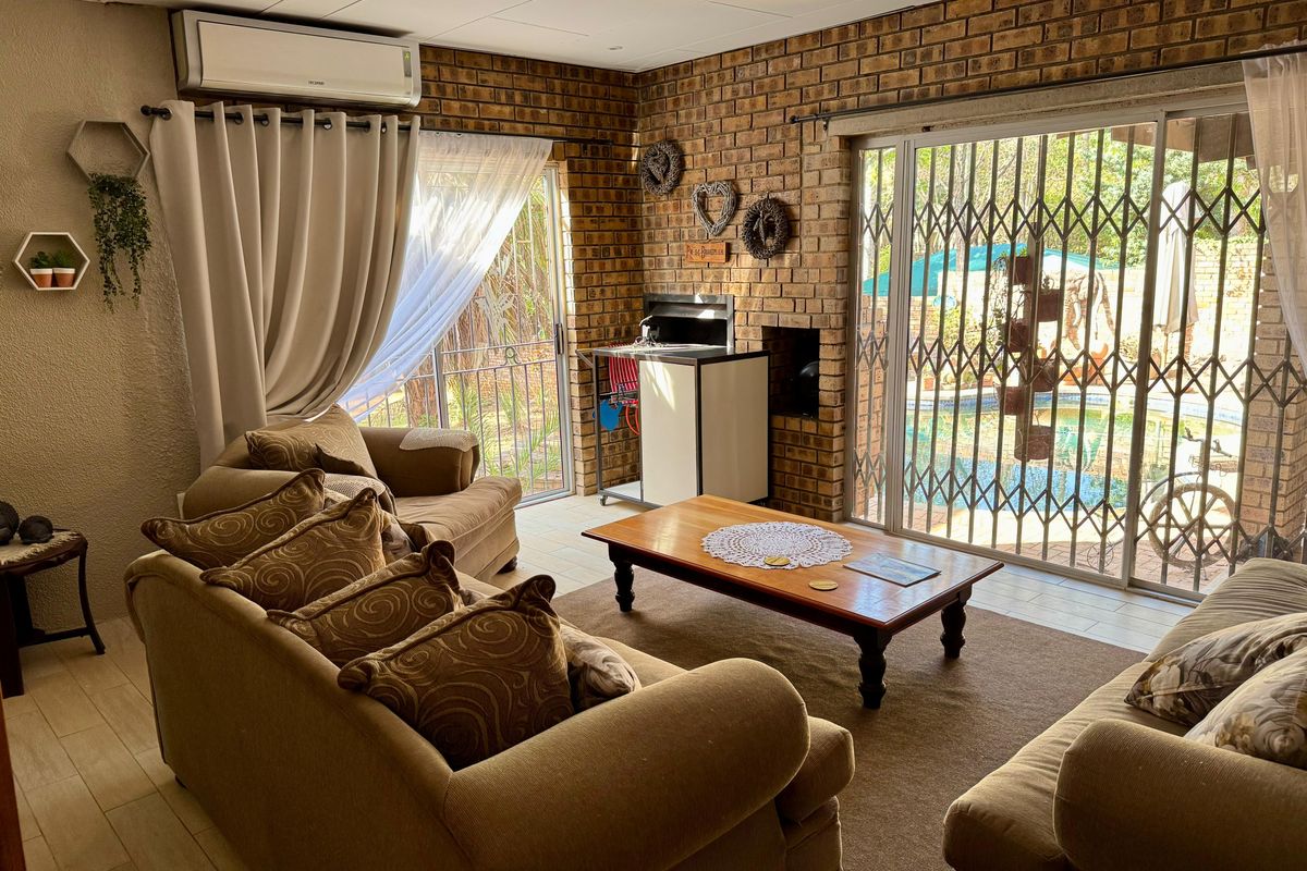 A cozy living room featuring exposed brick walls, a built-in braai, and sliding doors that open to the pool area.