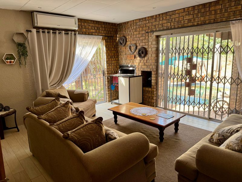 A cozy living room featuring exposed brick walls, a built-in braai, and sliding doors that open to the pool area.