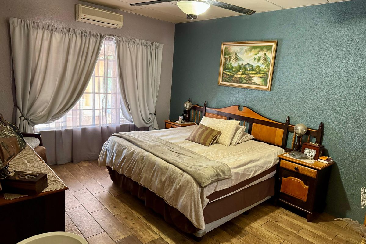 A comfortable bedroom featuring tiled flooring, a ceiling fan, and a wall-mounted split-system air conditioner for climate control.