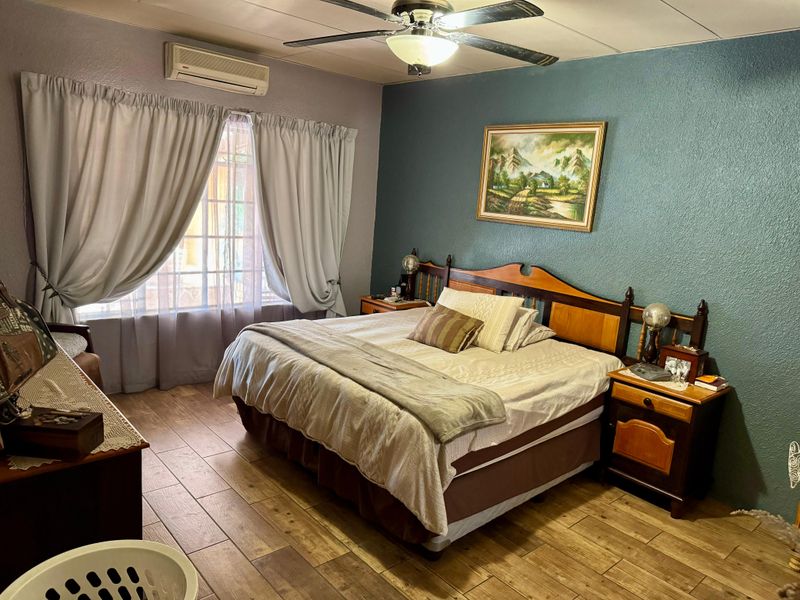 A comfortable bedroom featuring tiled flooring, a ceiling fan, and a wall-mounted split-system air conditioner for climate control.