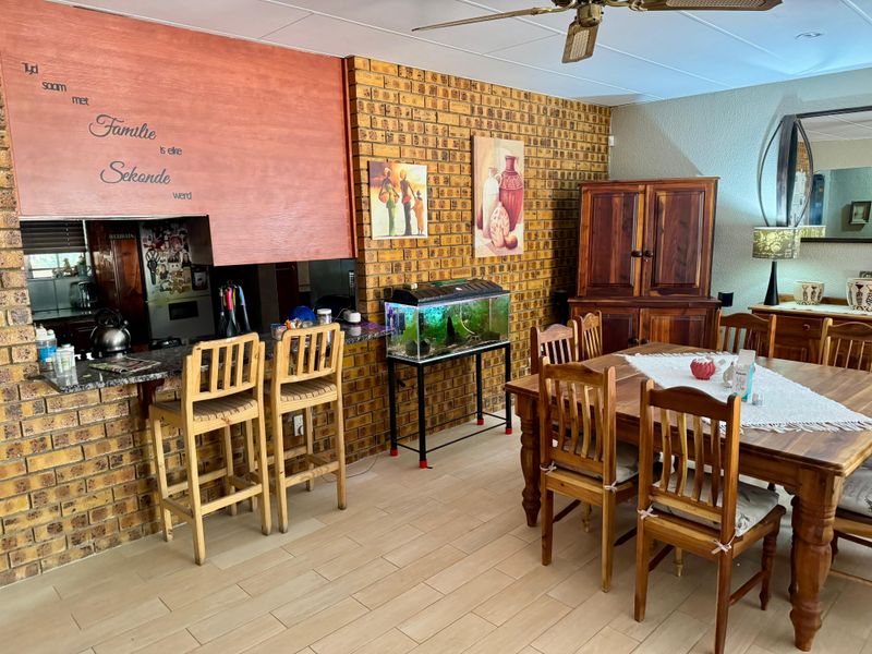 Open plan living and dining area featuring exposed brick walls, tiled flooring, and a breakfast bar connecting to the kitchen space.