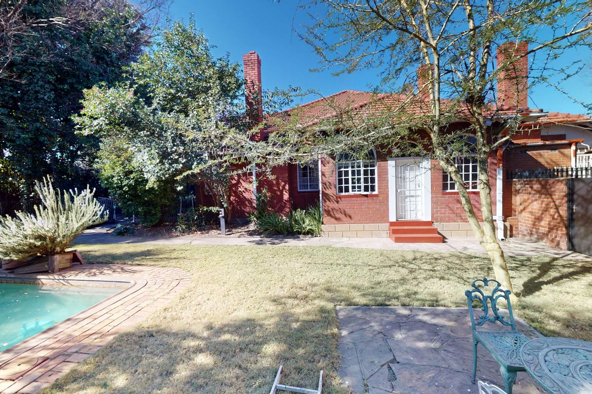 Rear view of a traditional brick house featuring a swimming pool, paved patio area, and established garden surroundings.