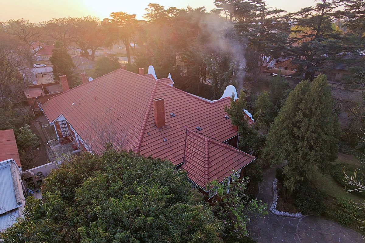 Aerial view of the property showcasing the tiled roof, brick chimneys, and surrounding mature garden and paved driveway area.