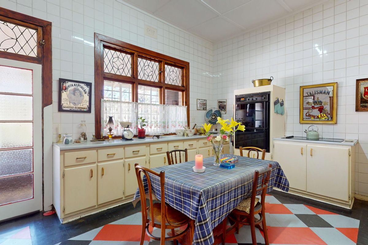 A vintage-style kitchen featuring original cabinetry, tiled walls, a built-in wall oven, and a leaded glass window, offering significant potential for modern renovation.