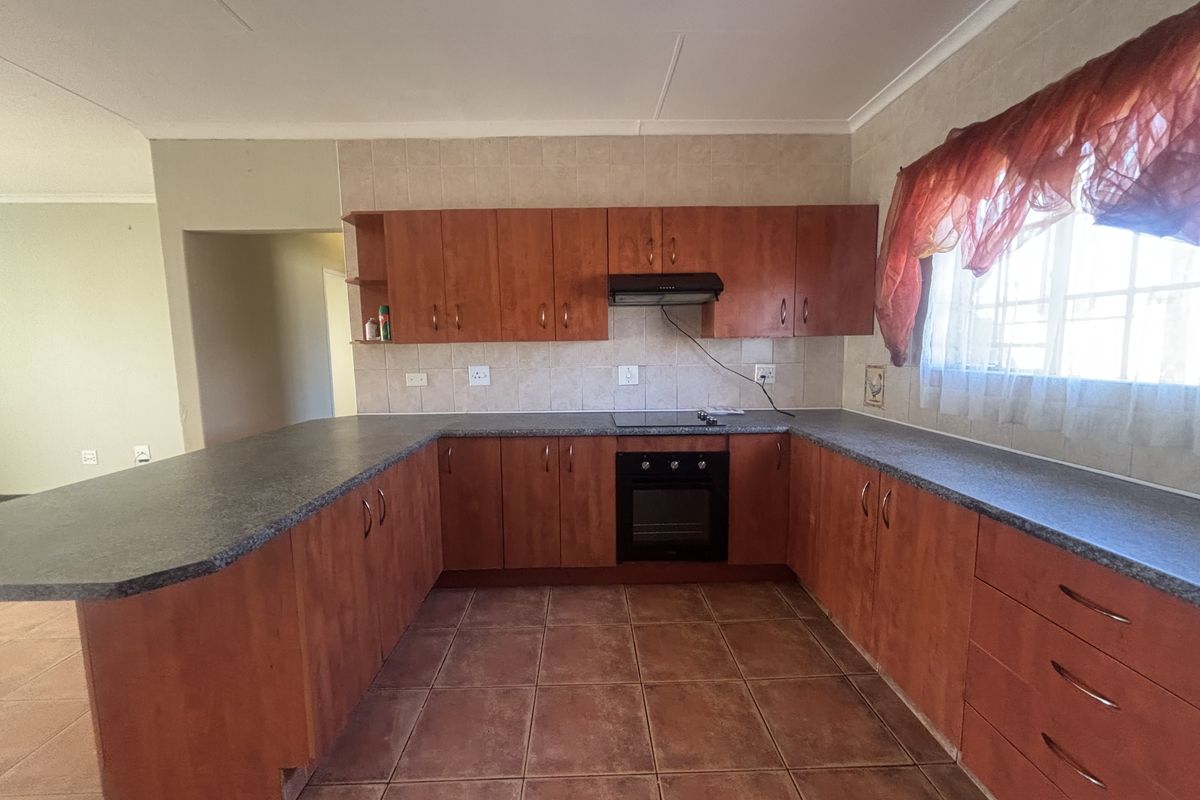 A functional U-shaped kitchen featuring wood-look cabinetry, dark laminate countertops, built-in oven and hob, and tiled flooring throughout.