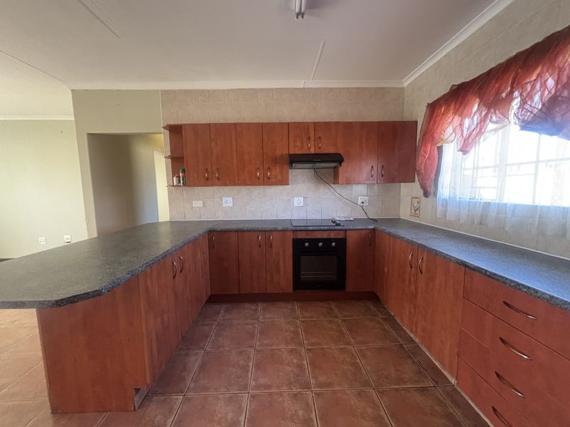 A functional U-shaped kitchen featuring wood-look cabinetry, dark laminate countertops, built-in oven and hob, and tiled flooring throughout.