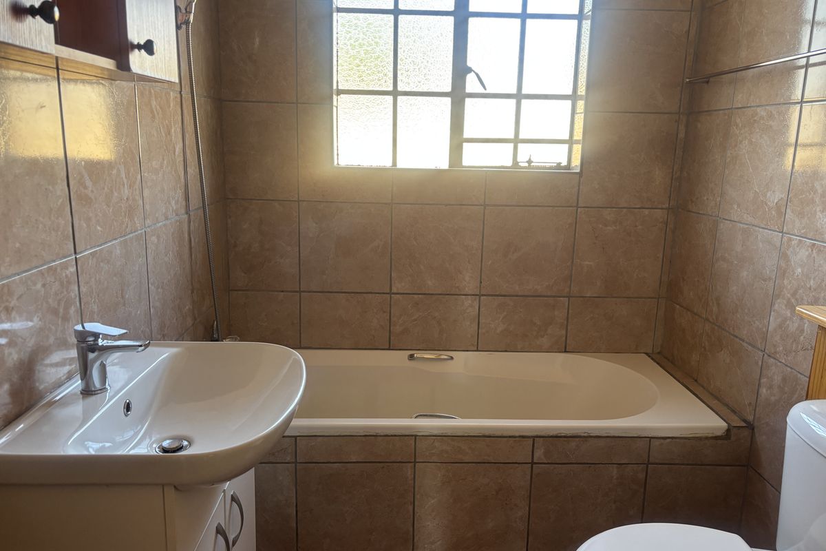 A functional bathroom featuring a built-in bathtub, vanity with basin, and full-height ceramic wall tiling.