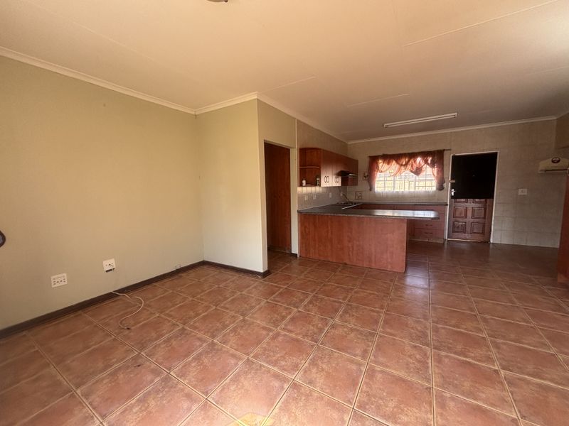 Open-plan living and kitchen area featuring tiled flooring, built-in wooden cabinetry, and a functional kitchen layout with a breakfast counter.