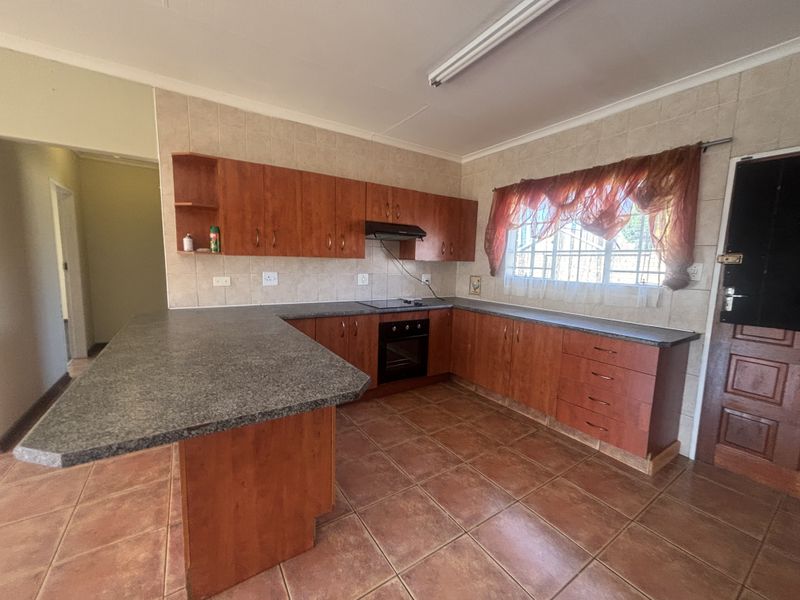 A functional kitchen featuring wooden cabinetry, laminate countertops, built-in oven, hob, and extractor fan, with tiled flooring and backsplash throughout.