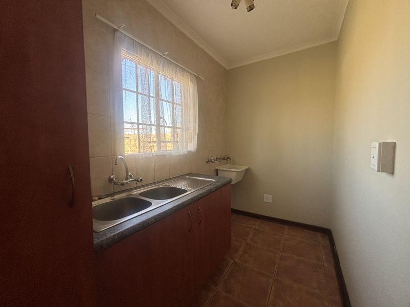 A functional laundry room featuring a double stainless steel sink, additional basin, tiled flooring, and built-in cabinetry for storage.