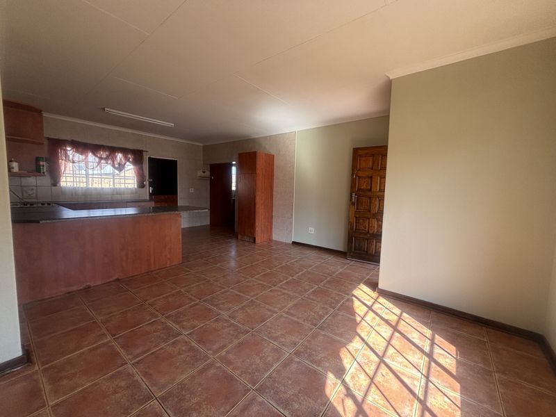 Spacious open-plan living and kitchen area featuring tiled flooring, built-in cabinetry, and a breakfast bar, offering a versatile layout for modern living.
