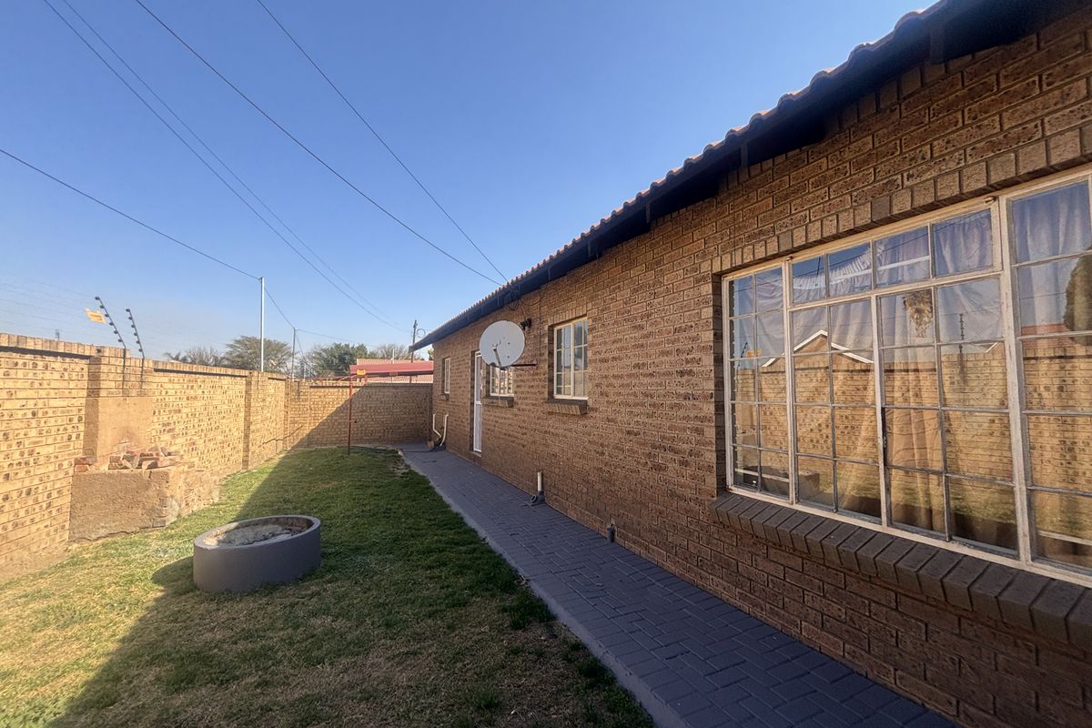 Rear exterior view of the townhouse featuring a face brick facade, paved walkway, and a private garden area enclosed by a perimeter wall.