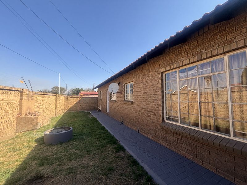 Rear exterior view of the townhouse featuring a face brick facade, paved walkway, and a private garden area enclosed by a perimeter wall.