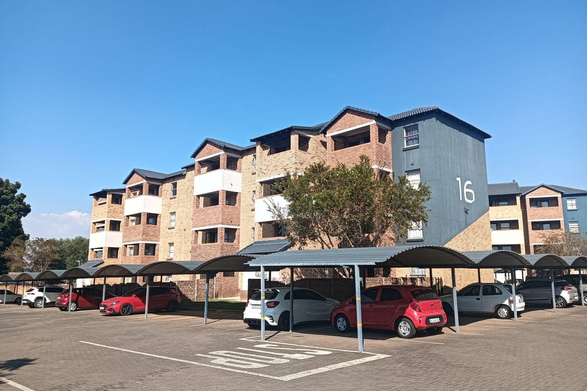 Exterior view of a multi-story apartment complex featuring facebrick architecture, tiled roofing, and dedicated covered parking bays for residents.