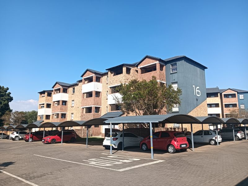 Exterior view of a multi-story apartment complex featuring facebrick architecture, tiled roofing, and dedicated covered parking bays for residents.