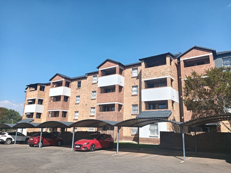 Exterior view of a multi-story apartment complex featuring face brick construction, private balconies, and dedicated covered parking bays.