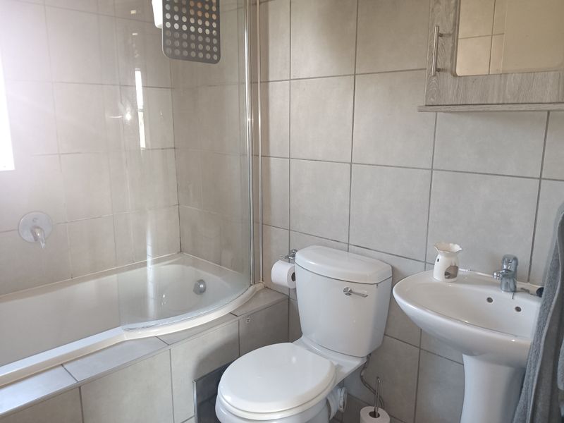 A functional bathroom featuring a bathtub with a glass shower screen, a pedestal basin, and a wall-mounted medicine cabinet with neutral wall tiling.
