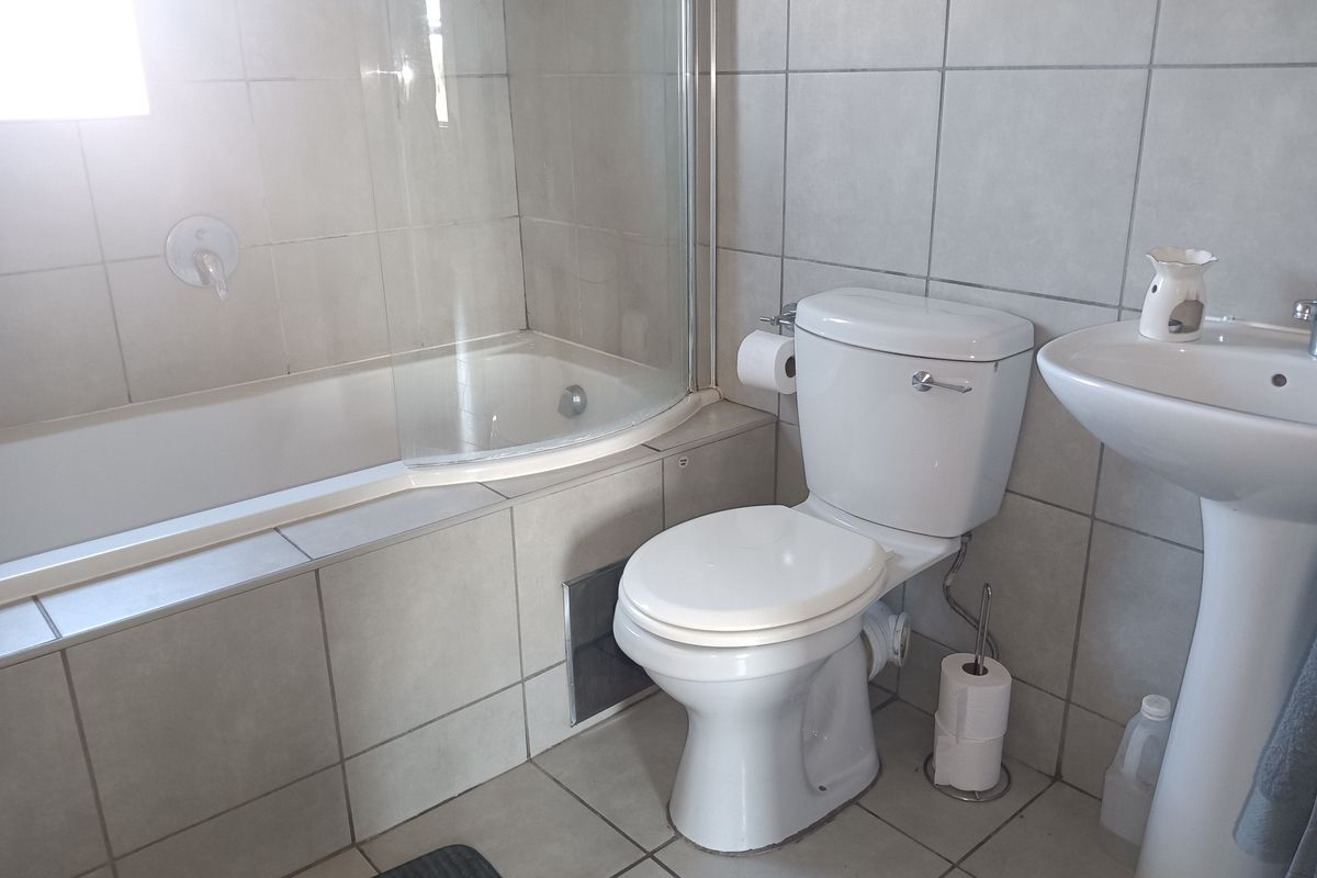 A functional bathroom featuring a bathtub with a glass screen, a pedestal basin, and neutral ceramic tiling throughout.