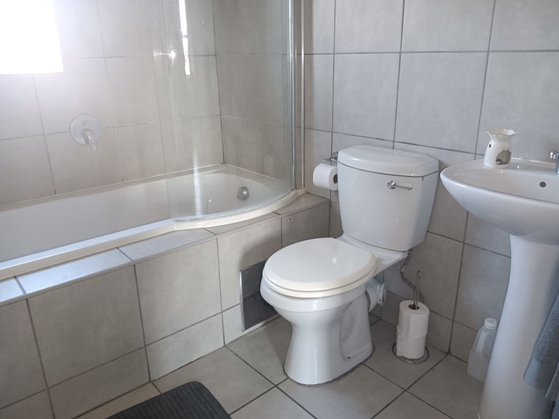 A functional bathroom featuring a bathtub with a glass screen, a pedestal basin, and neutral ceramic tiling throughout.