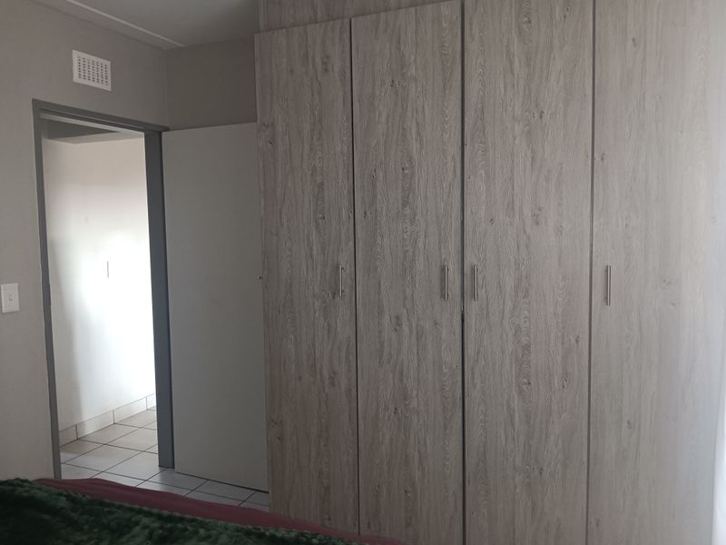 A bedroom featuring modern wood-grain built-in cupboards and a doorway leading to an adjacent tiled area.