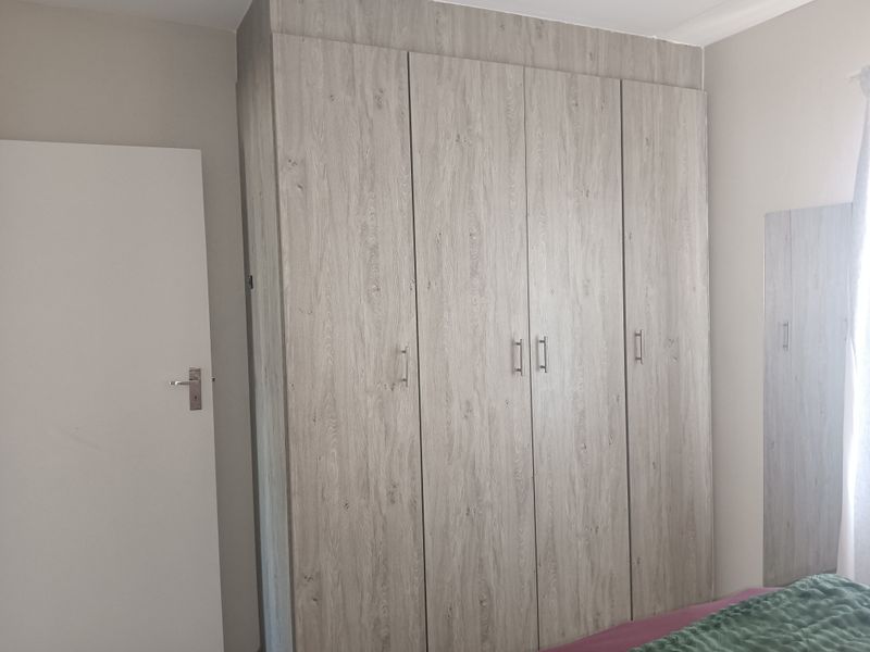 A bedroom featuring a modern, light wood-grain built-in wardrobe with sleek metal handles.