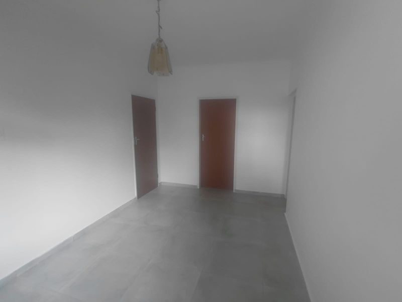 A vacant, neutral hallway featuring grey floor tiles and two internal doors, providing a clean and simple transition space within the home.