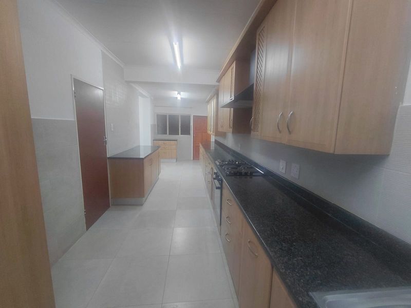 A spacious, empty galley-style kitchen featuring light wood cabinetry, dark granite countertops, a gas hob, and tiled flooring.
