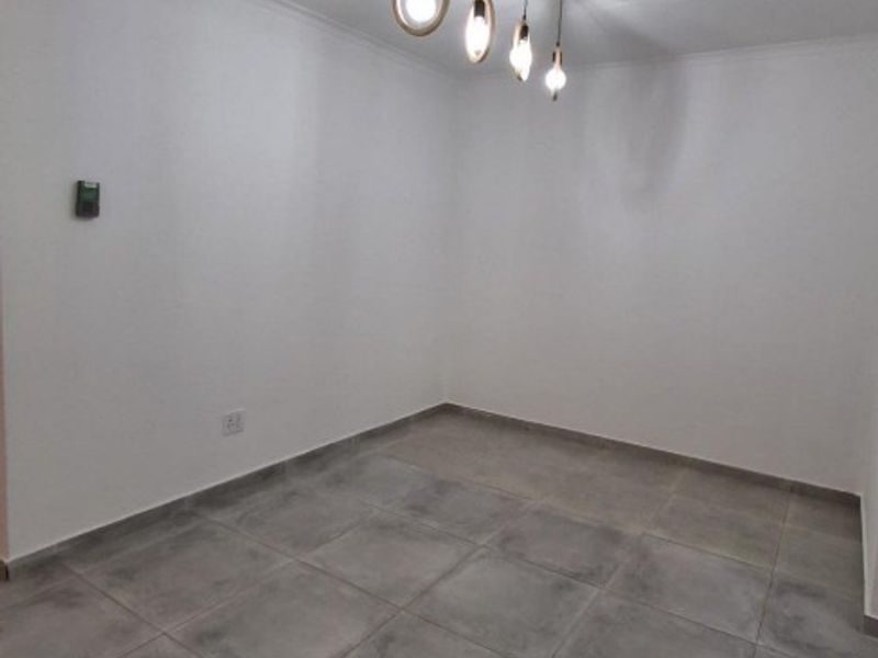 A clean, empty living space featuring modern grey floor tiles and a contemporary four-light pendant fixture.
