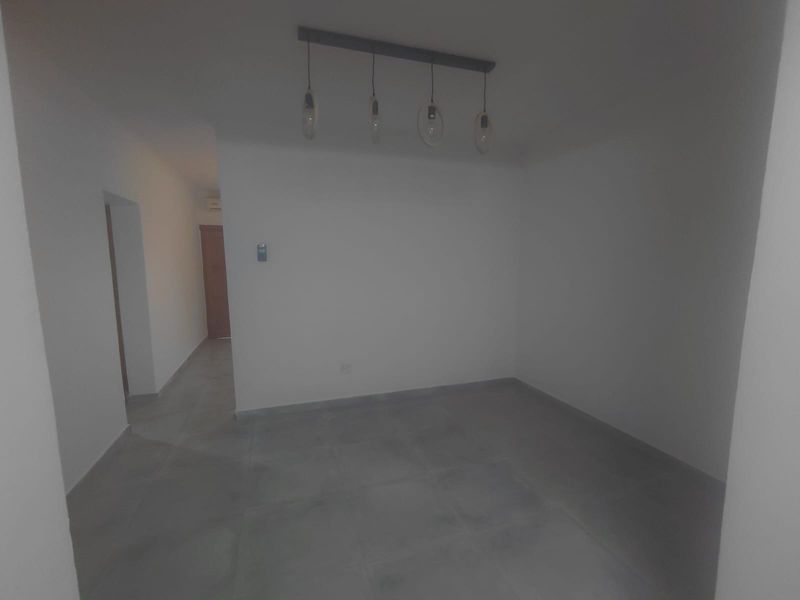 An empty, neutral living area featuring modern tiled flooring and a contemporary pendant light fixture, offering a blank canvas for interior design.