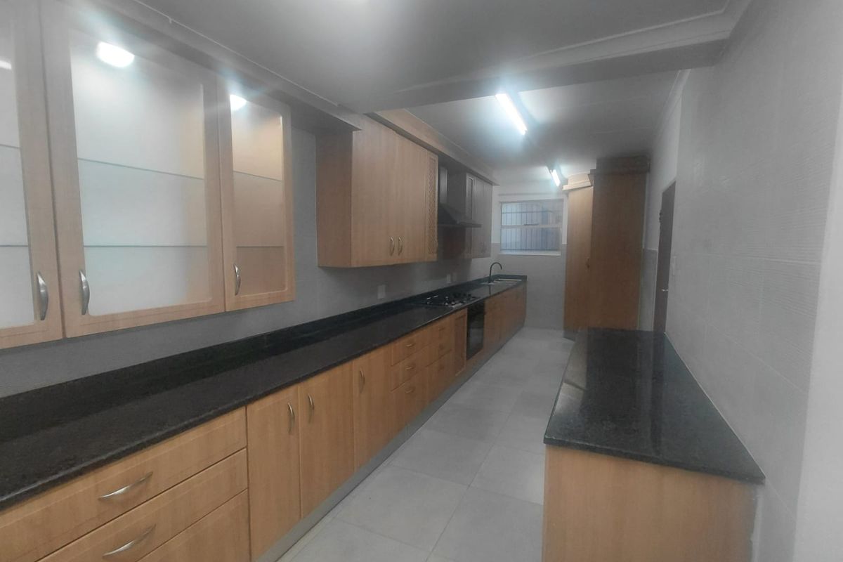 A spacious, functional kitchen featuring extensive wooden cabinetry, granite countertops, built-in oven, gas hob, and tiled flooring.
