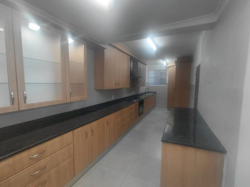 A spacious, functional kitchen featuring extensive wooden cabinetry, granite countertops, built-in oven, gas hob, and tiled flooring.