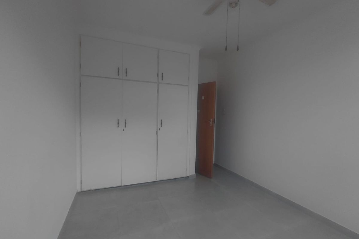 An empty bedroom featuring built-in cupboards, a ceiling fan, and neutral tiled flooring.