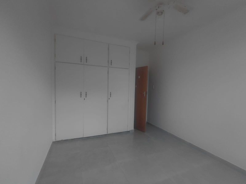 An empty bedroom featuring built-in cupboards, a ceiling fan, and neutral tiled flooring.
