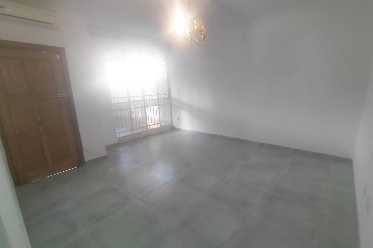 An empty living room featuring tiled flooring, a split-system air conditioner, and a security gate leading to the exterior.
