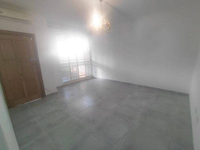 An empty living room featuring tiled flooring, a split-system air conditioner, and a security gate leading to the exterior.