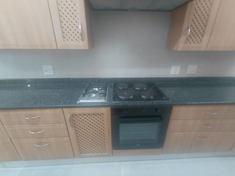 A functional kitchen area featuring light wood-finish cabinetry, granite countertops, and a combination of gas and electric hobs with a built-in oven.