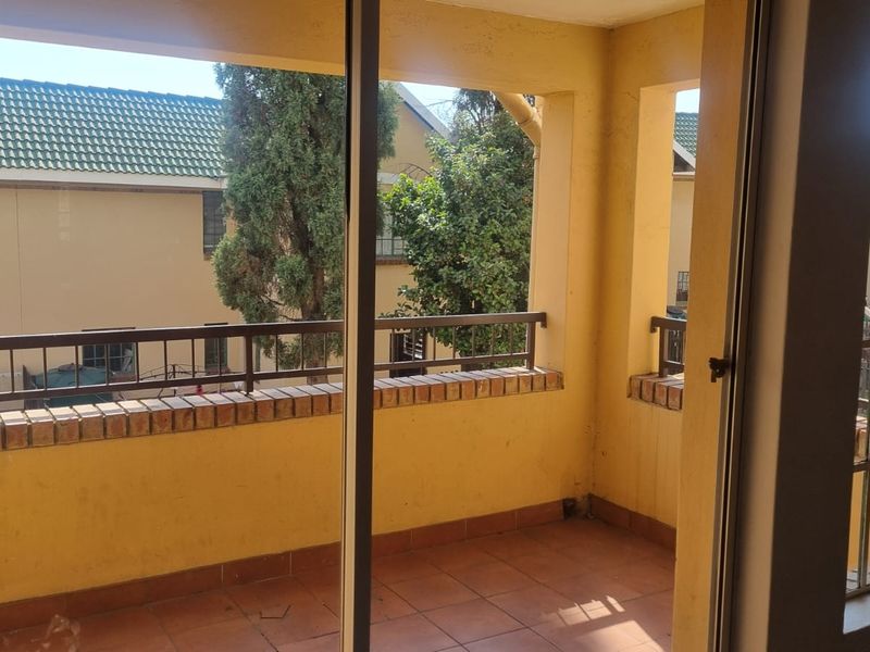 A covered balcony featuring tiled flooring, a brick balustrade with metal railing, and sliding glass door access, offering a view of the surrounding complex.