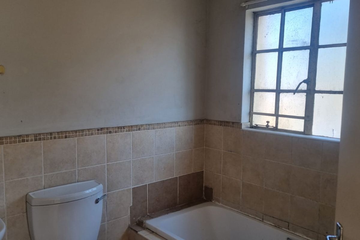 A dated bathroom featuring a bathtub, toilet, and partial wall tiling, currently in need of renovation and cosmetic repairs.